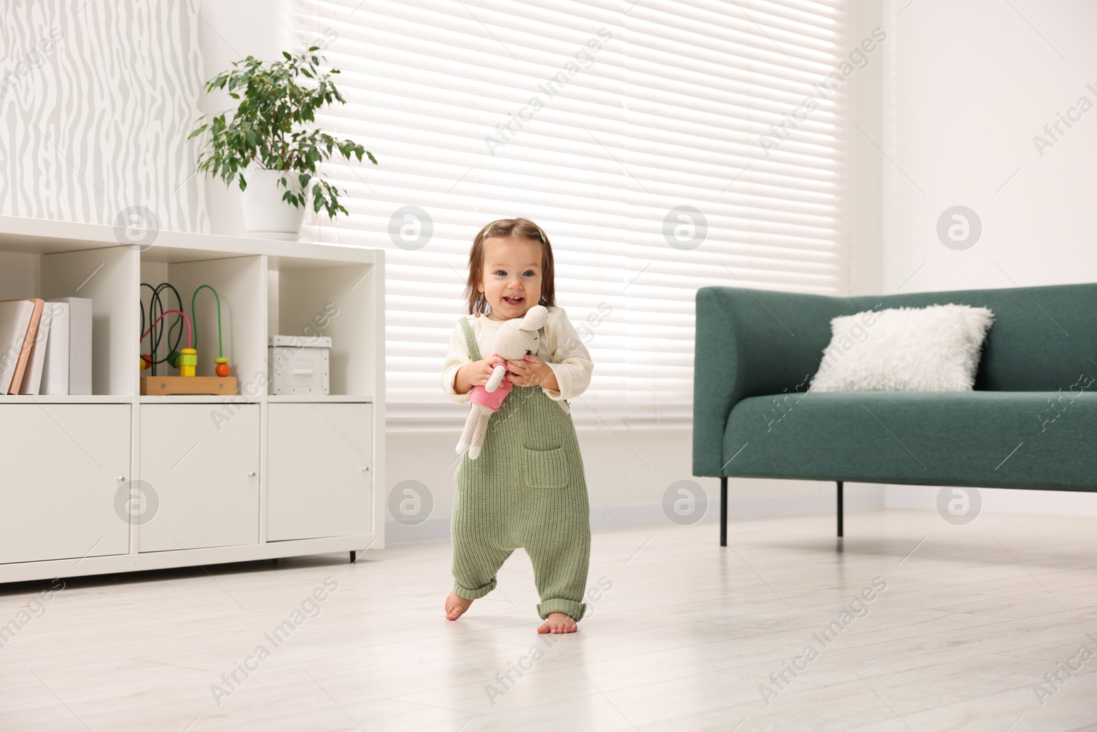 Photo of First steps. Cute little baby with toy learning to walk at home