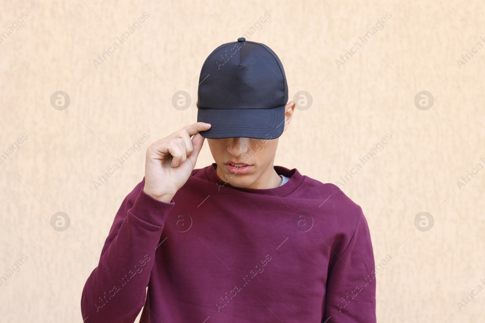 Photo of Man in stylish baseball cap near beige wall. Mockup for design