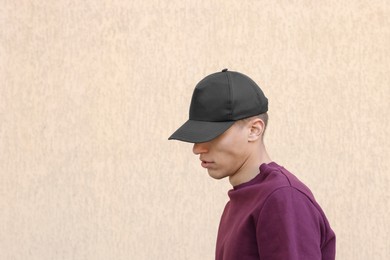 Photo of Man in stylish baseball cap near beige wall. Mockup for design