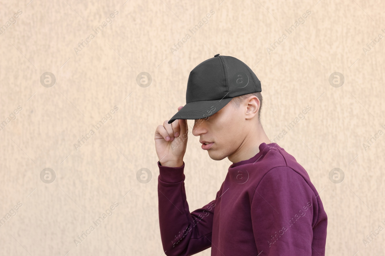 Photo of Man in stylish baseball cap near beige wall. Mockup for design