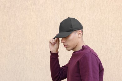 Man in stylish baseball cap near beige wall. Mockup for design