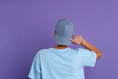 Photo of Man in stylish baseball cap on violet background, back view. Mockup for design