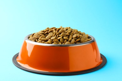 Photo of Dry pet food in feeding bowl on light blue background