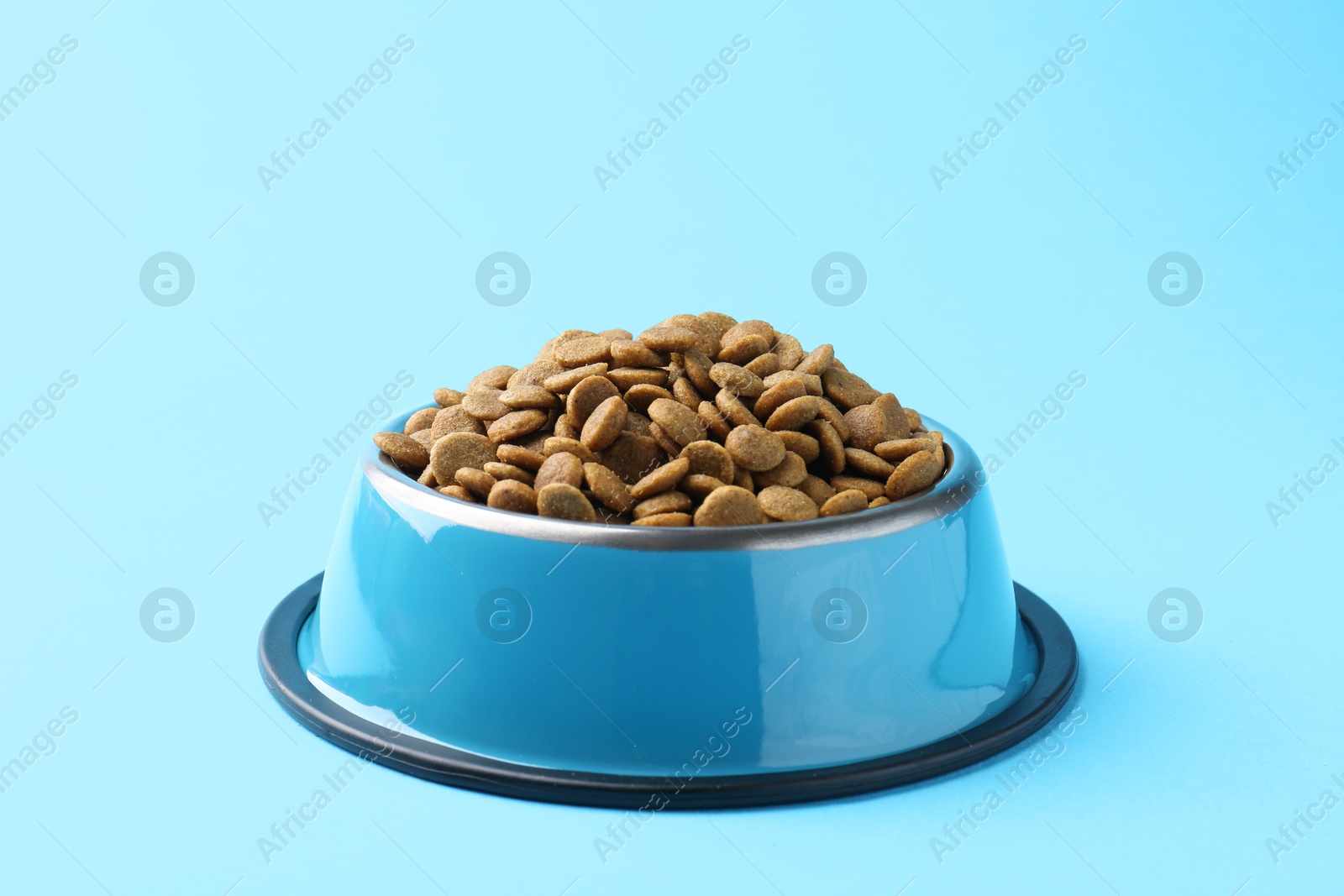 Photo of Dry pet food in feeding bowl on light blue background