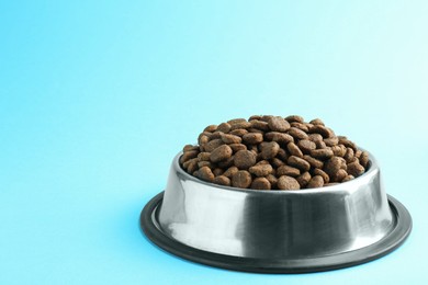 Photo of Dry pet food in feeding bowl on light blue background. Space for text