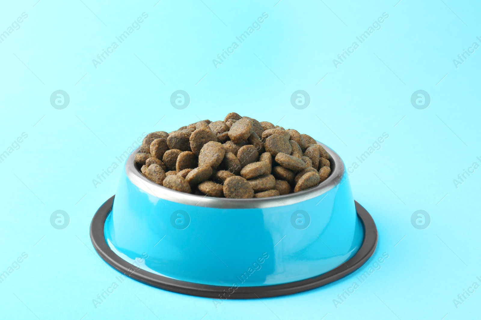 Photo of Dry pet food in feeding bowl on light blue background