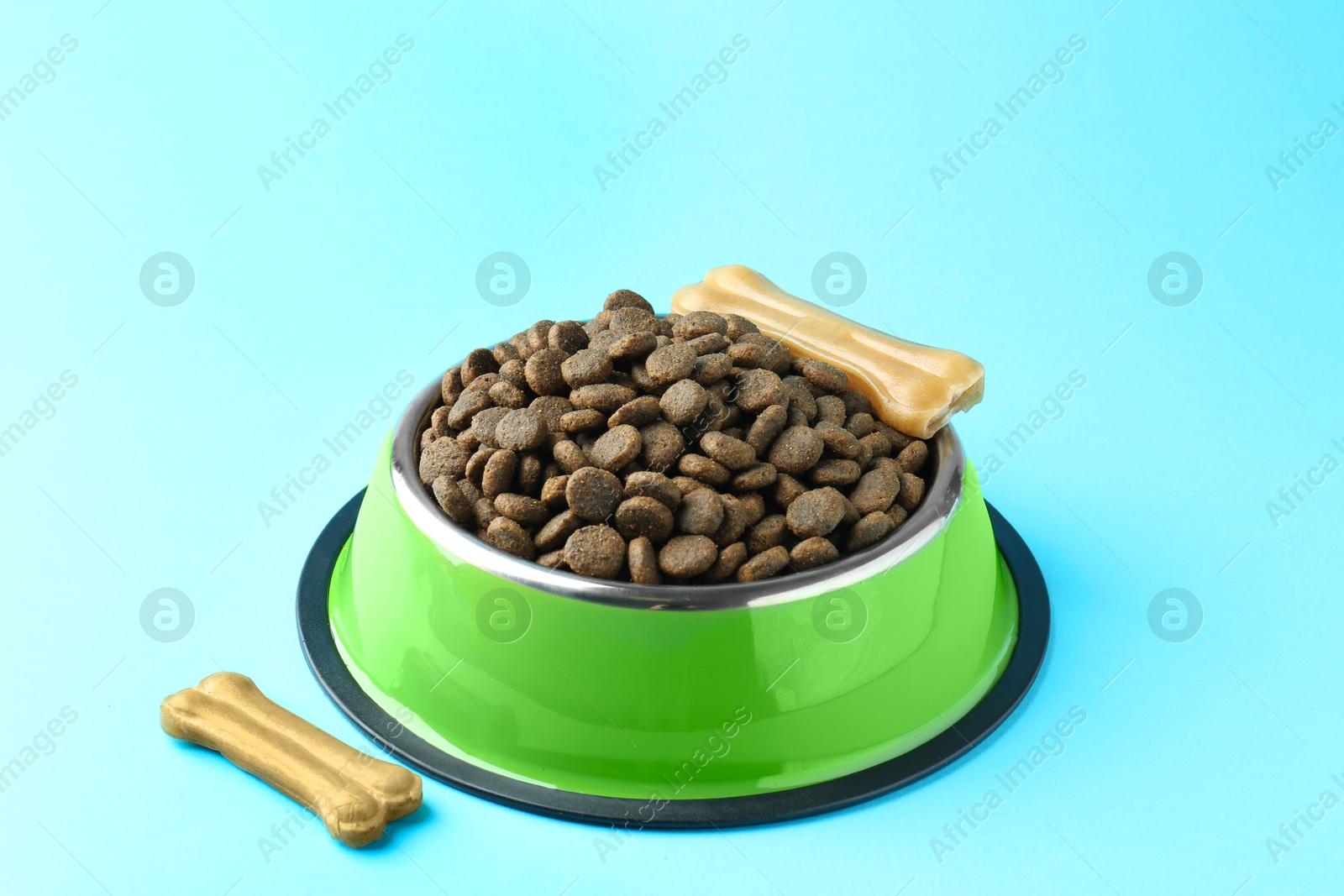 Photo of Dry pet food in feeding bowl and chew bones on light blue background