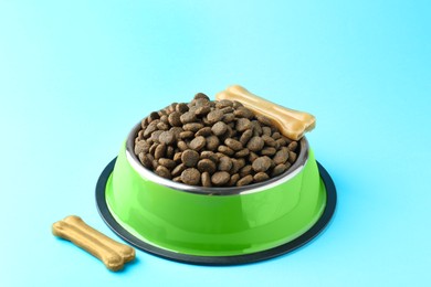 Photo of Dry pet food in feeding bowl and chew bones on light blue background