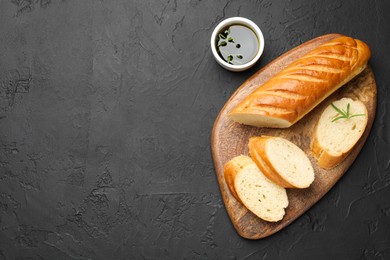 Photo of Cut fresh baguette with balsamic and rosemary on black table, top view. Space for text