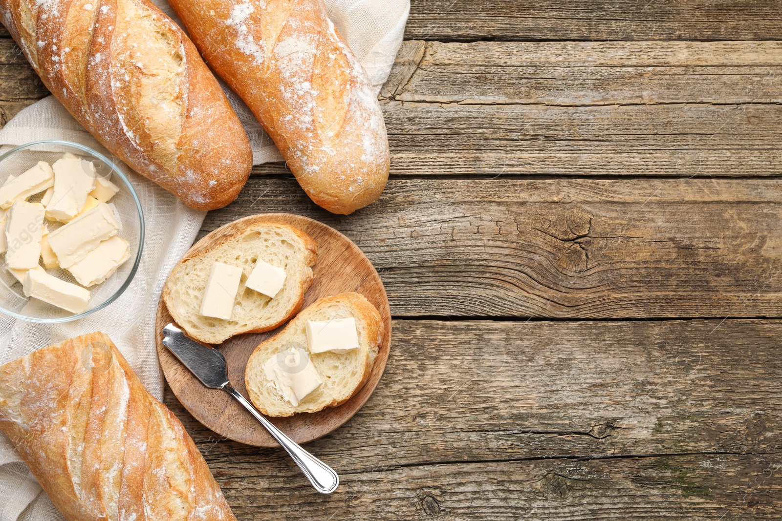 Photo of Slices of fresh baguette with butter on wooden table, flat lay. Space for text