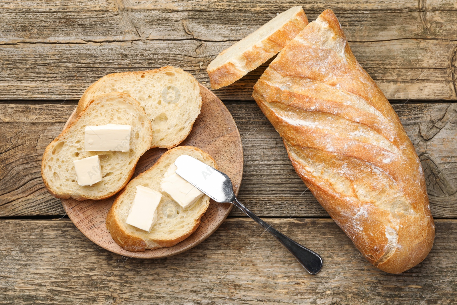 Photo of Slices of fresh baguette with butter on wooden table, flat lay