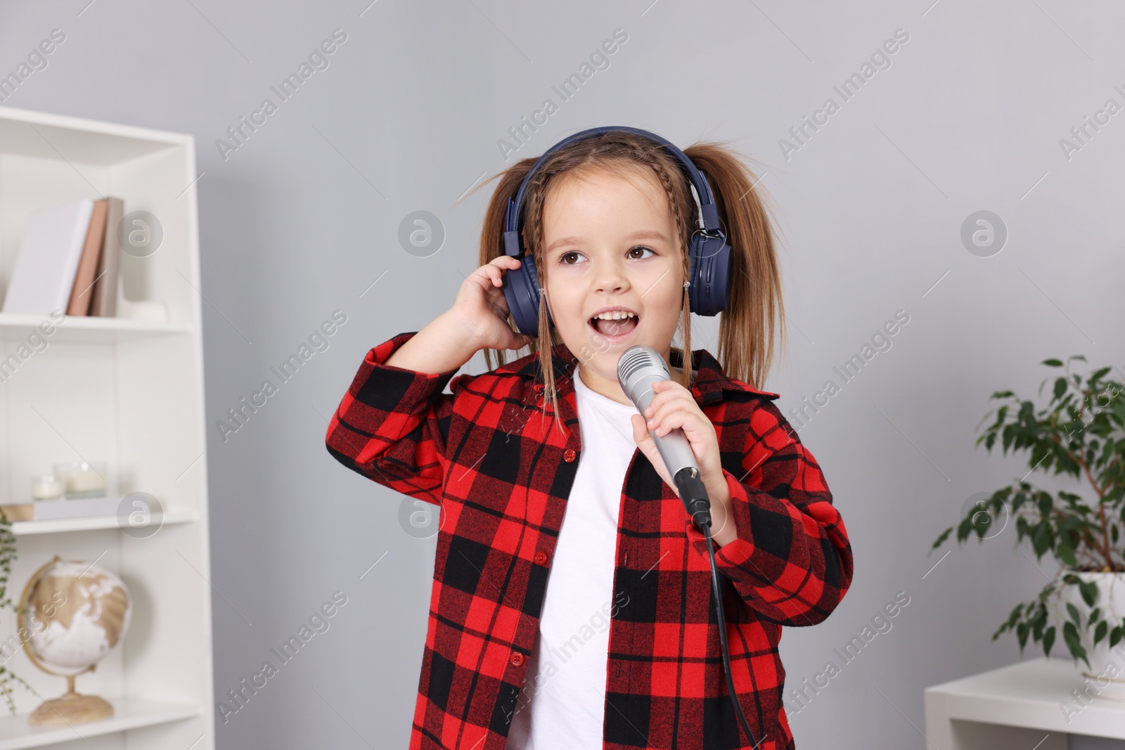 Photo of Cute girl with microphone in headphones singing at home