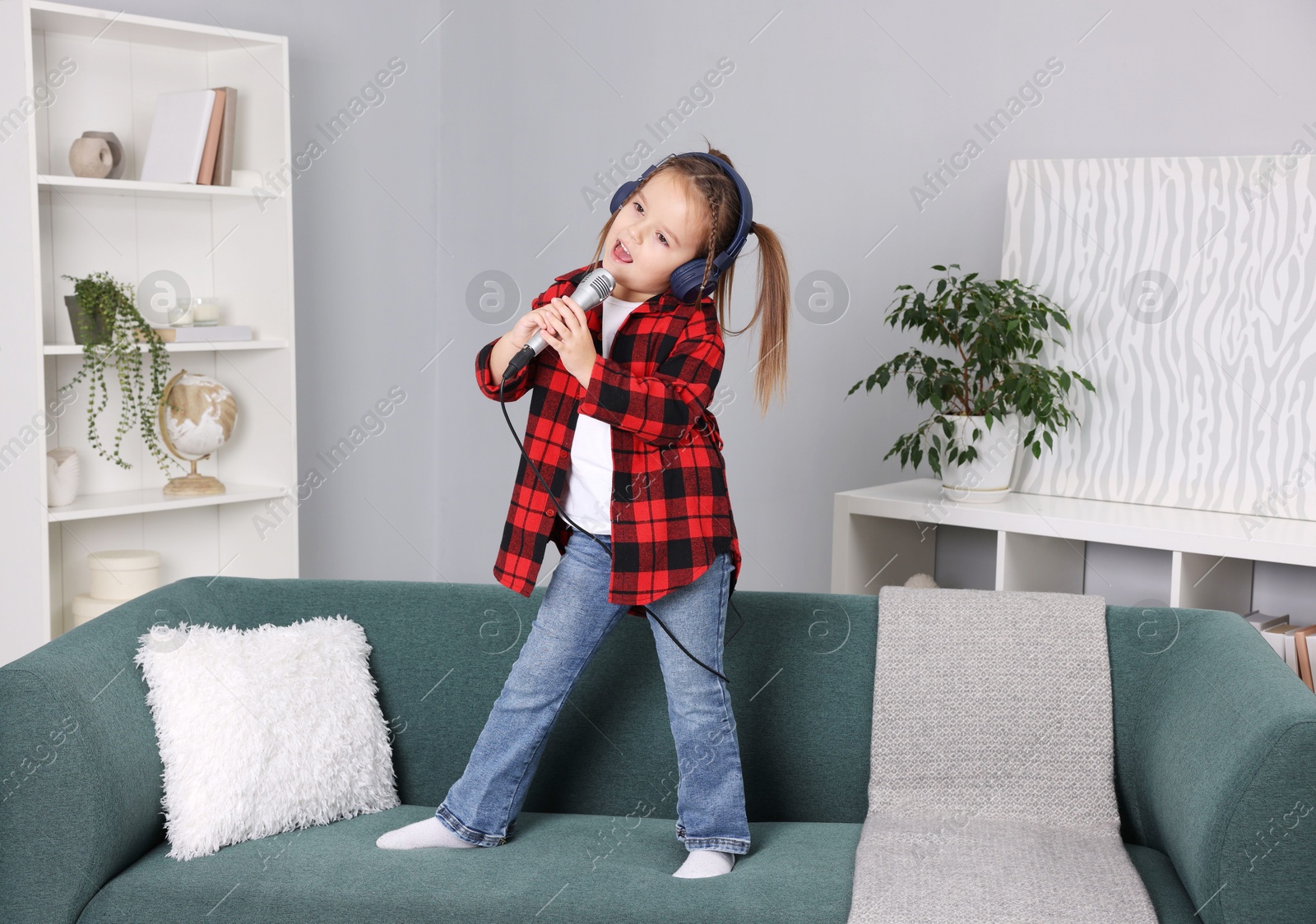 Photo of Cute girl with microphone in headphones singing on sofa at home