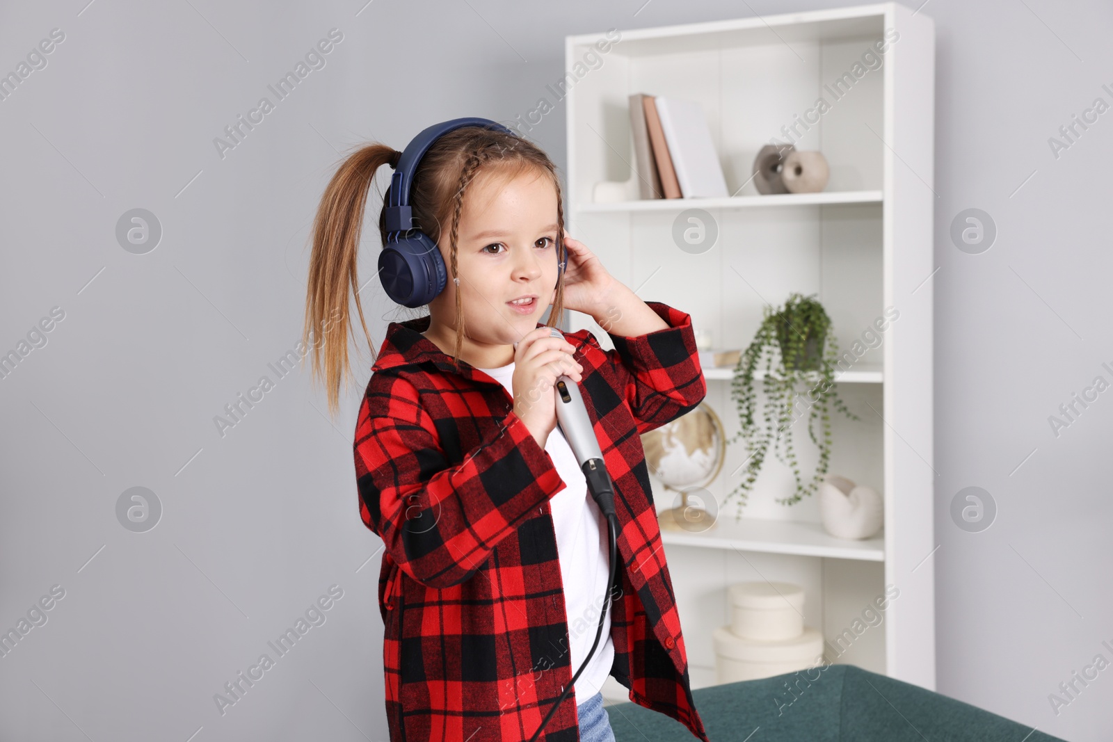 Photo of Cute girl with microphone in headphones singing at home