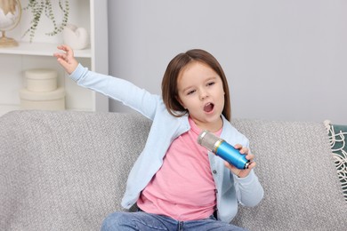 Photo of Cute girl with microphone singing on sofa at home