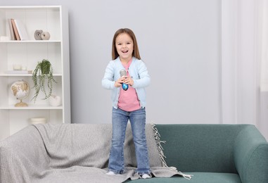 Photo of Cute girl with microphone singing on sofa at home