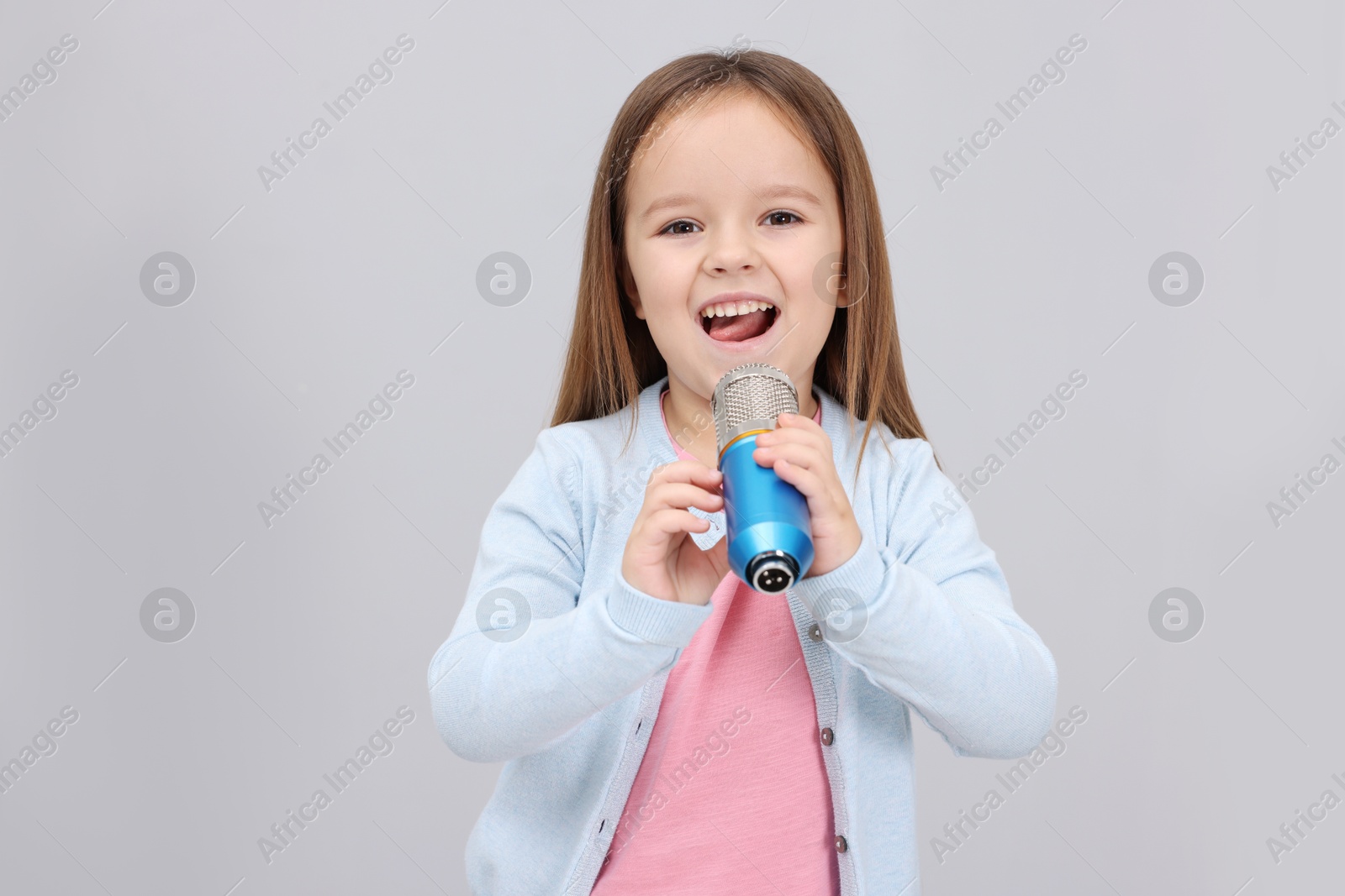 Photo of Cute girl with microphone singing near grey wall