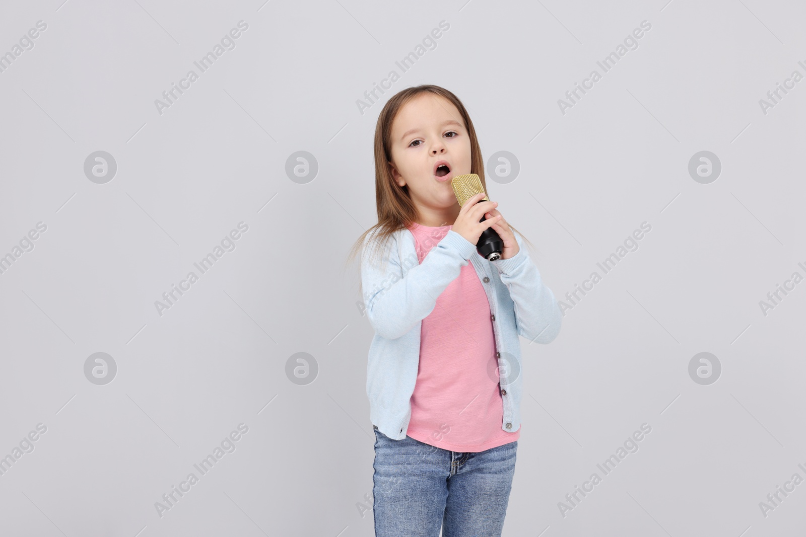 Photo of Cute girl with microphone singing near grey wall