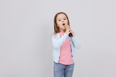 Photo of Cute girl with microphone singing near grey wall