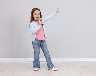 Photo of Cute girl with microphone singing near grey wall