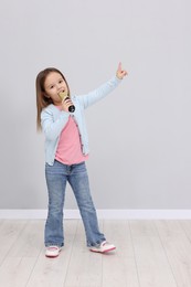 Photo of Cute girl with microphone singing near grey wall