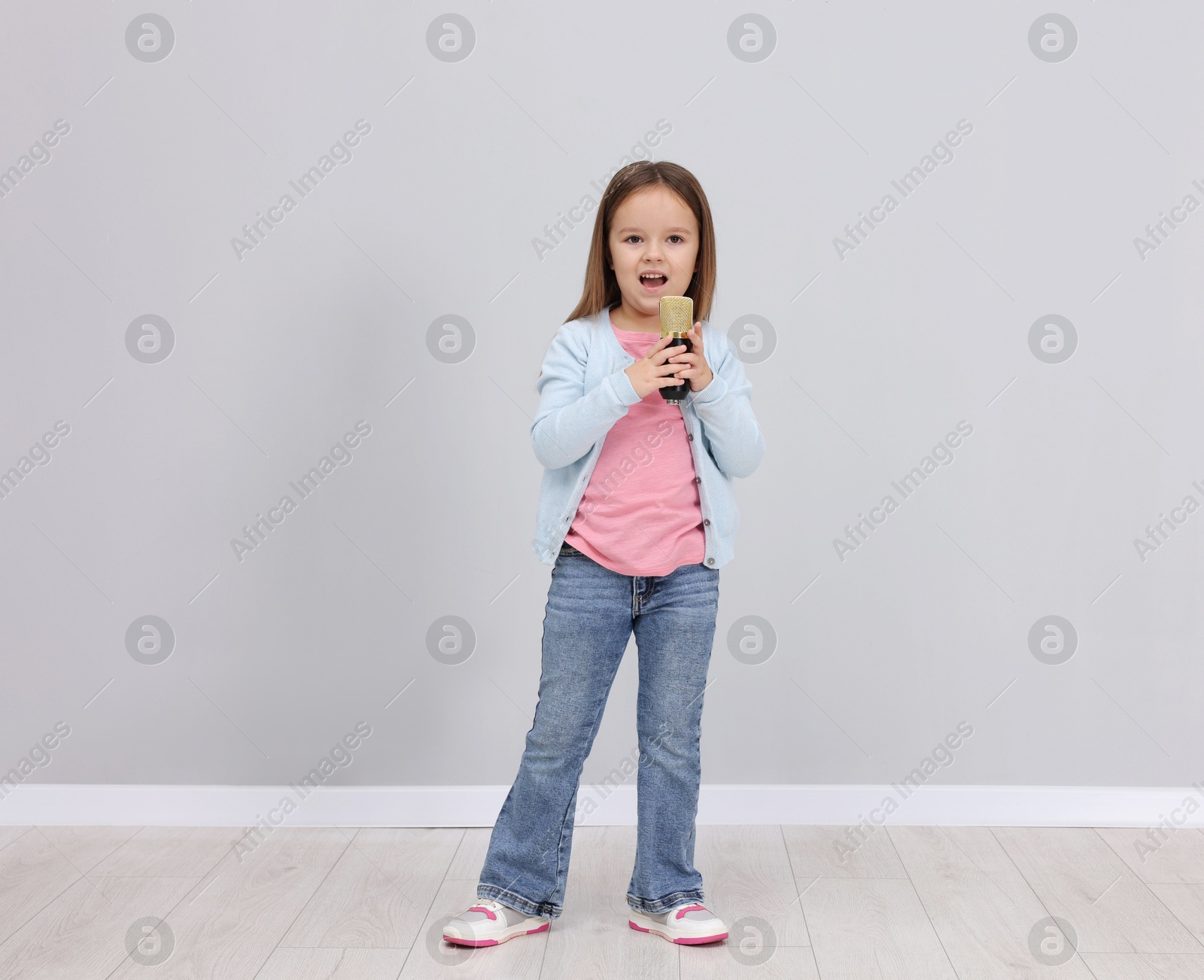 Photo of Cute girl with microphone singing near grey wall