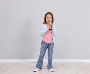 Photo of Cute girl with microphone singing near grey wall