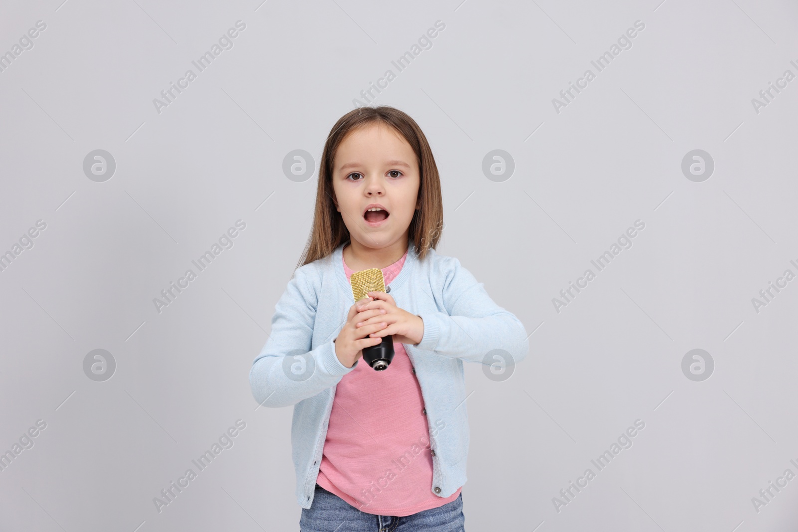 Photo of Cute girl with microphone singing near grey wall