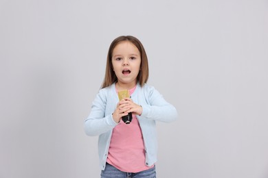 Photo of Cute girl with microphone singing near grey wall