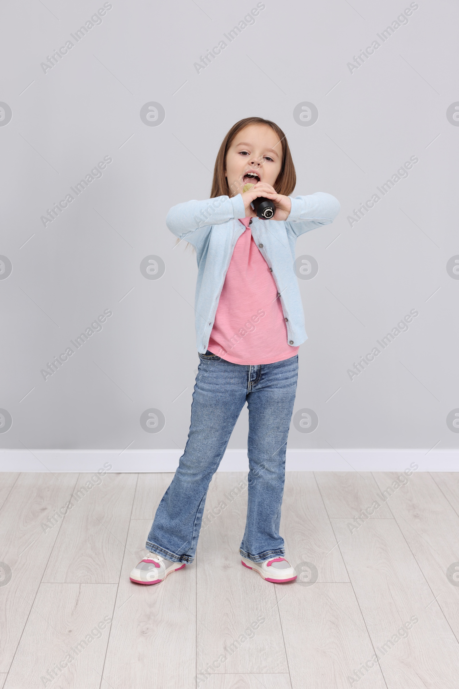 Photo of Cute girl with microphone singing near grey wall