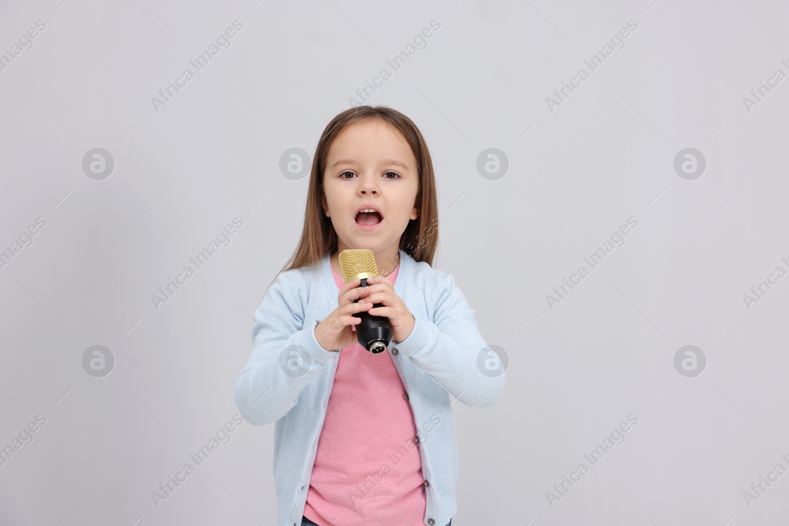 Photo of Cute girl with microphone singing near grey wall