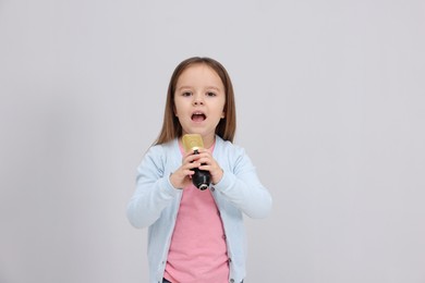 Photo of Cute girl with microphone singing near grey wall