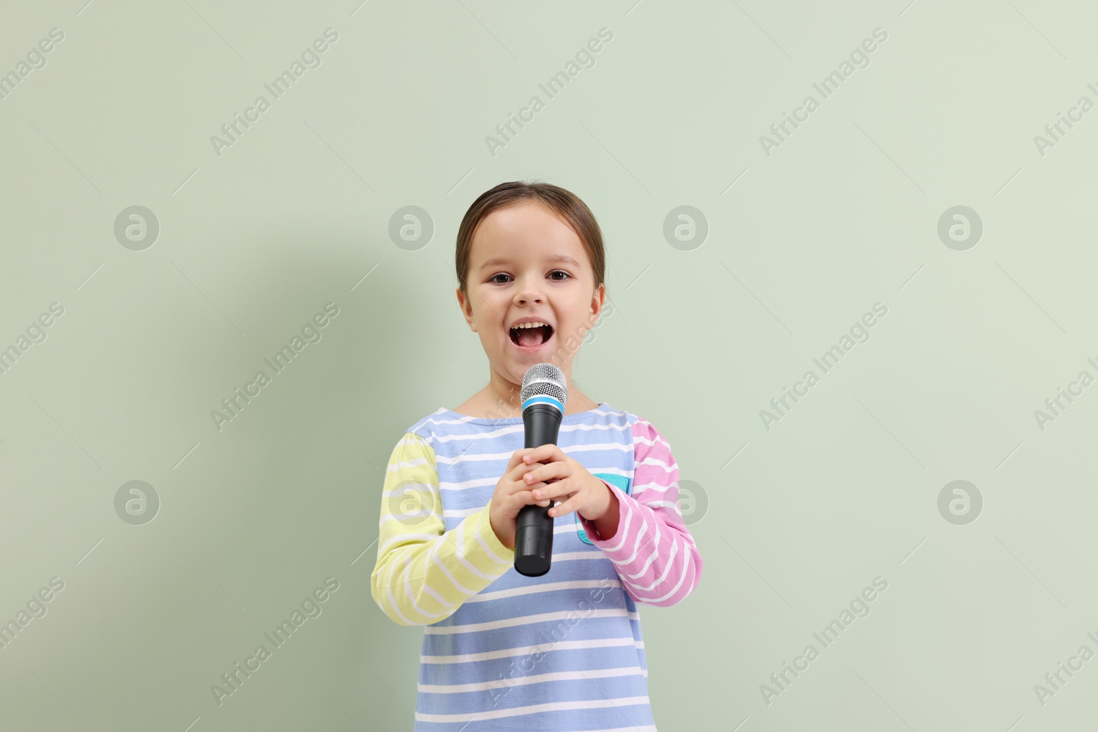 Photo of Cute girl with microphone singing near green wall