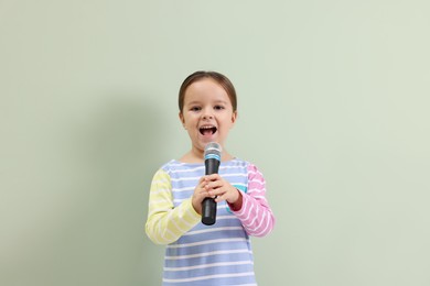 Photo of Cute girl with microphone singing near green wall