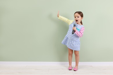 Photo of Cute girl with microphone singing near green wall. Space for text