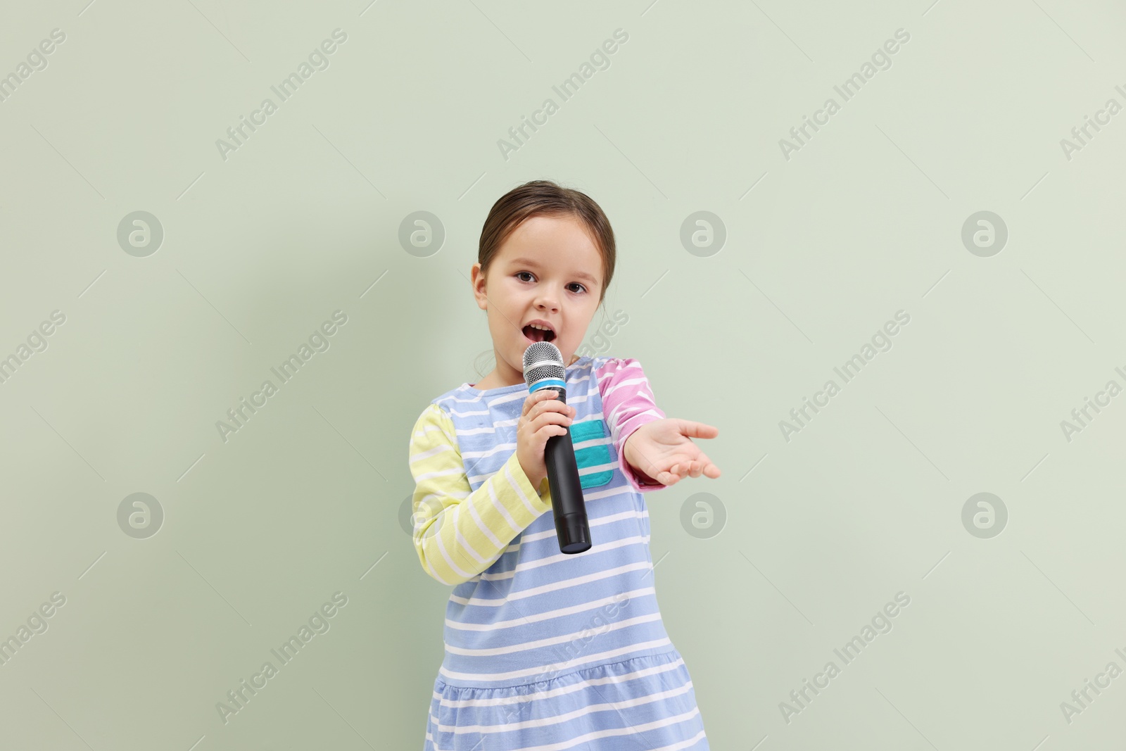 Photo of Cute girl with microphone singing near green wall