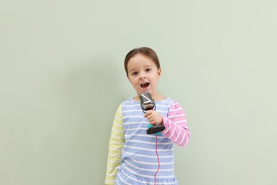 Photo of Cute girl with microphone singing near green wall