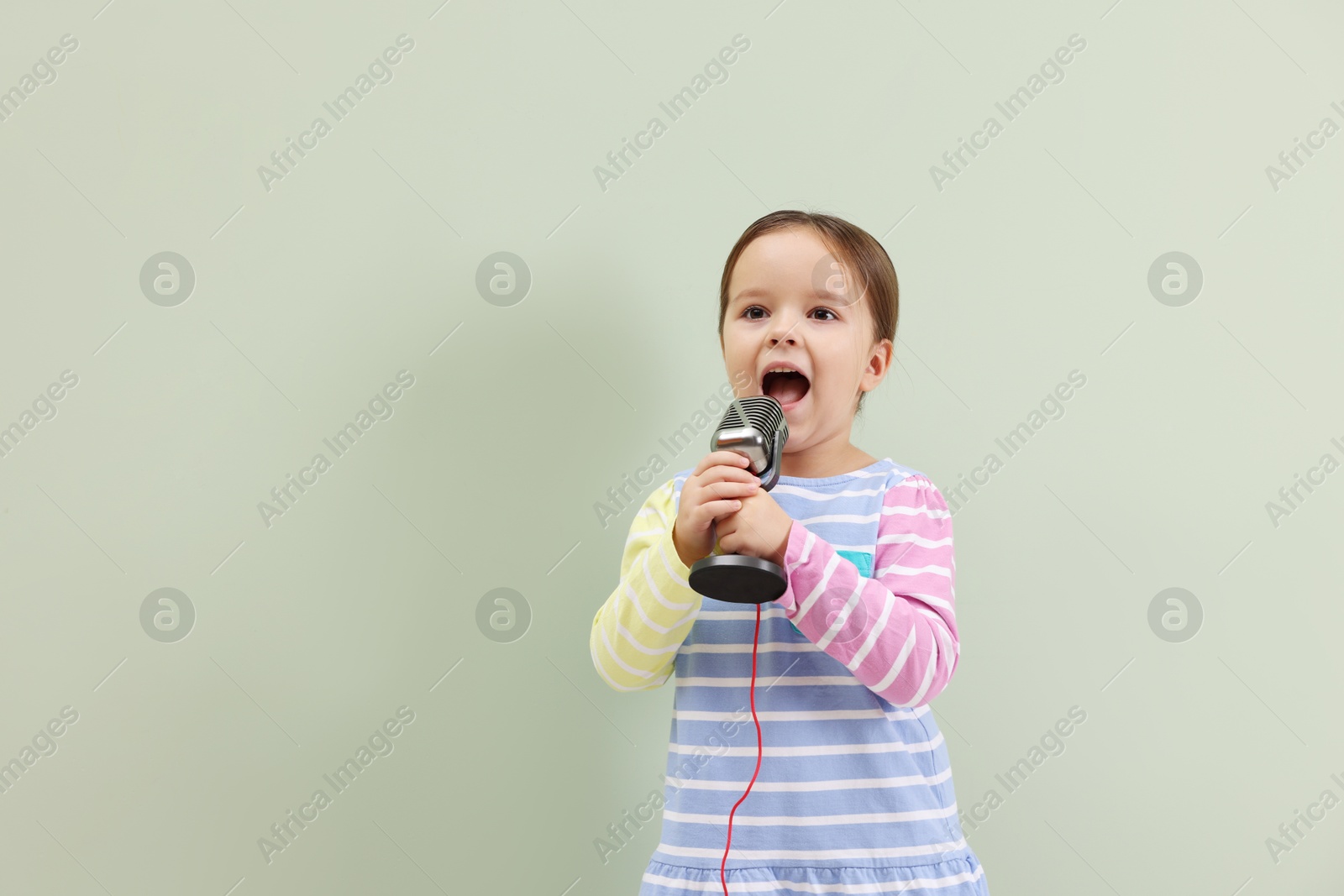 Photo of Cute girl with microphone singing near green wall. Space for text