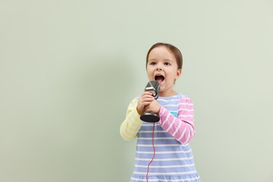 Photo of Cute girl with microphone singing near green wall. Space for text