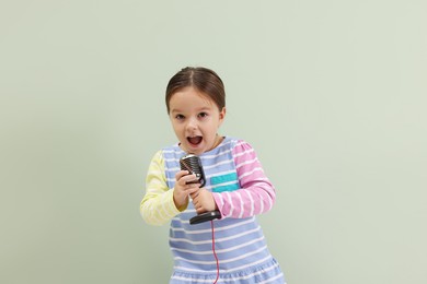 Photo of Cute girl with microphone singing near green wall