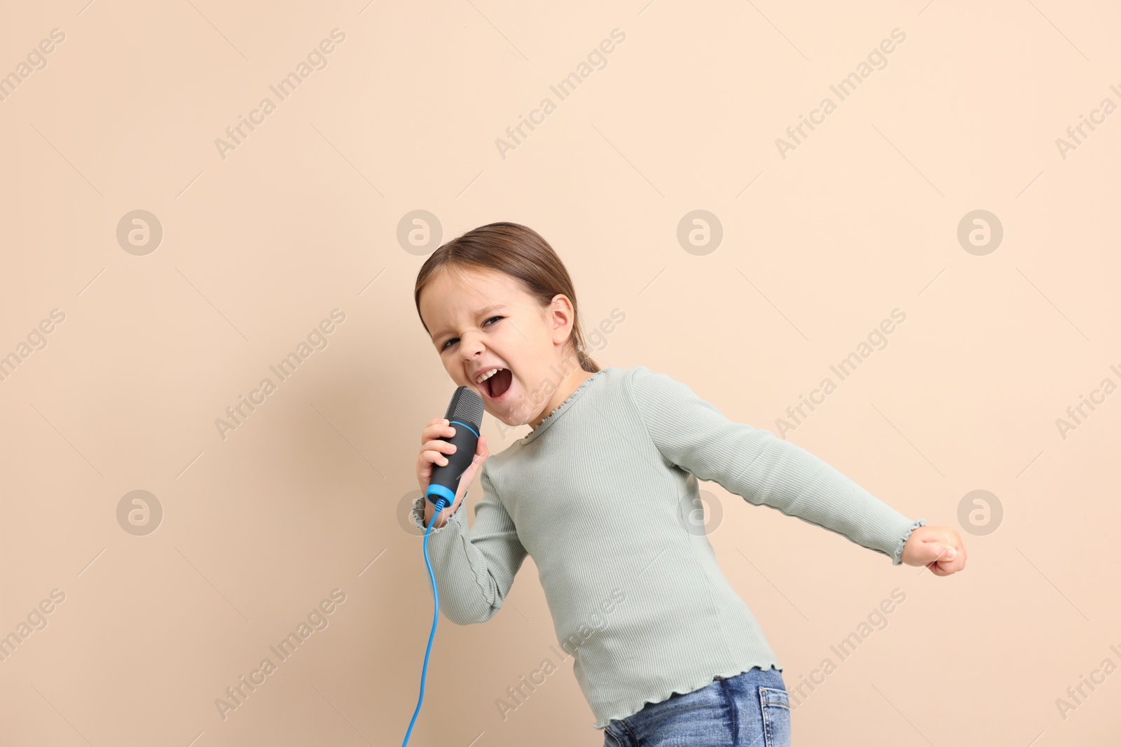 Photo of Cute girl with microphone singing near beige wall