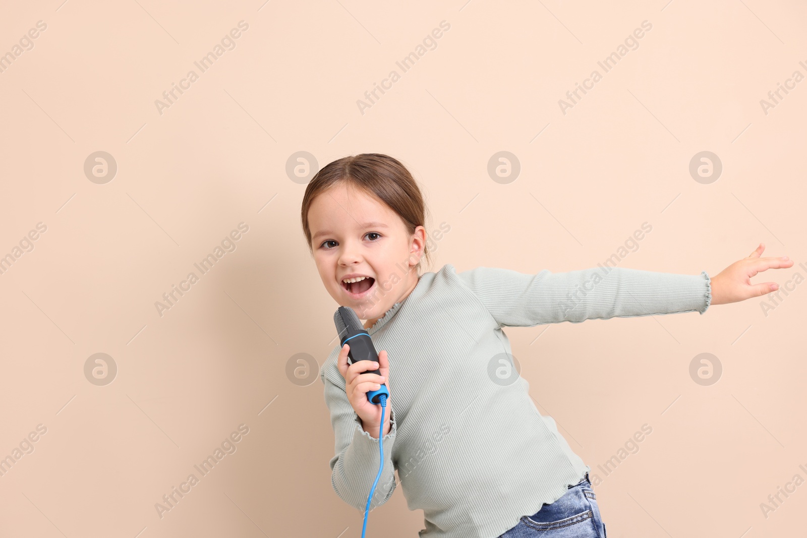 Photo of Cute girl with microphone singing near beige wall. Space for text