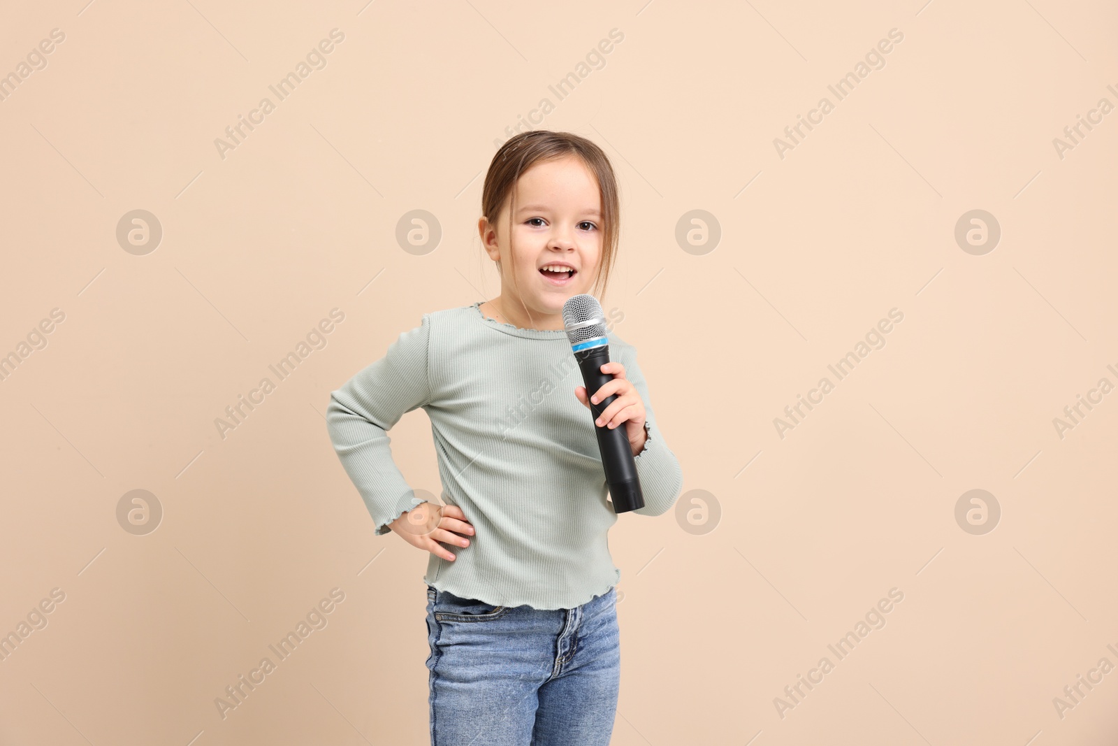 Photo of Cute girl with microphone singing near beige wall