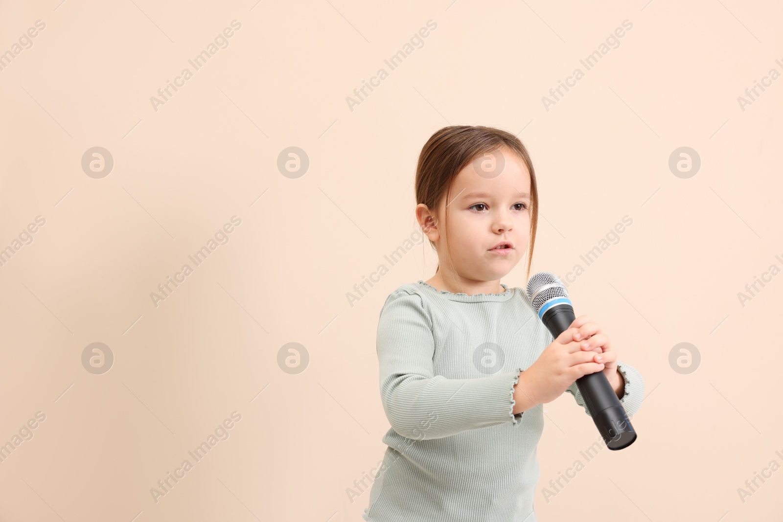 Photo of Cute girl with microphone singing near beige wall. Space for text