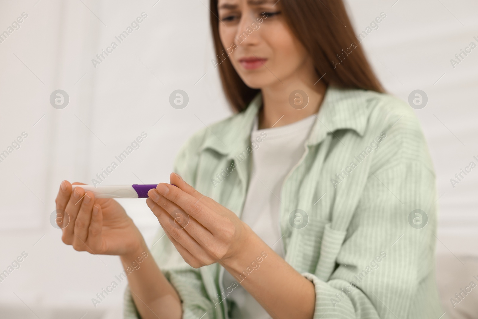 Photo of Upset woman with negative pregnancy test at home, selective focus