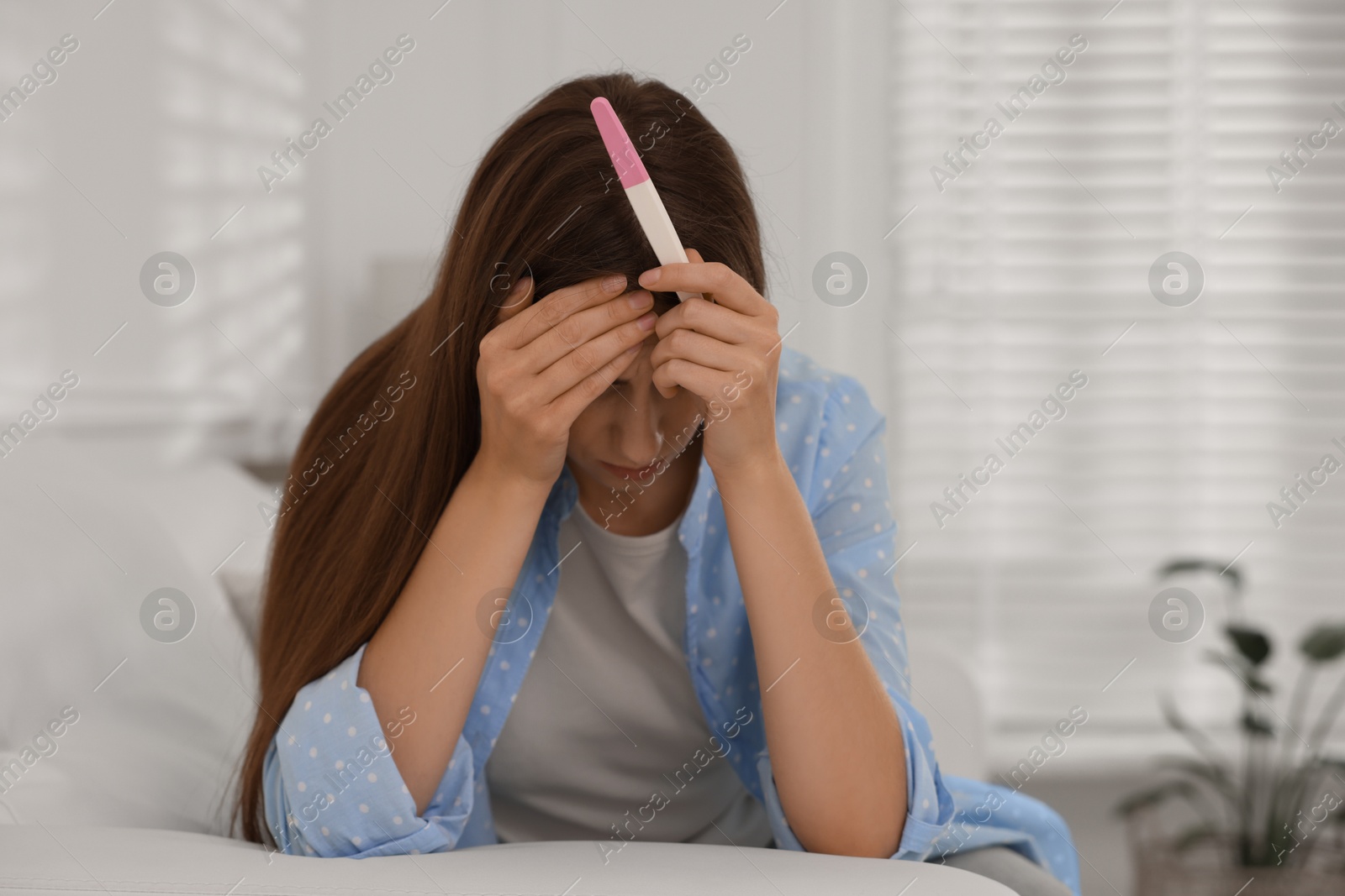 Photo of Upset woman with negative pregnancy test on sofa at home, space for text