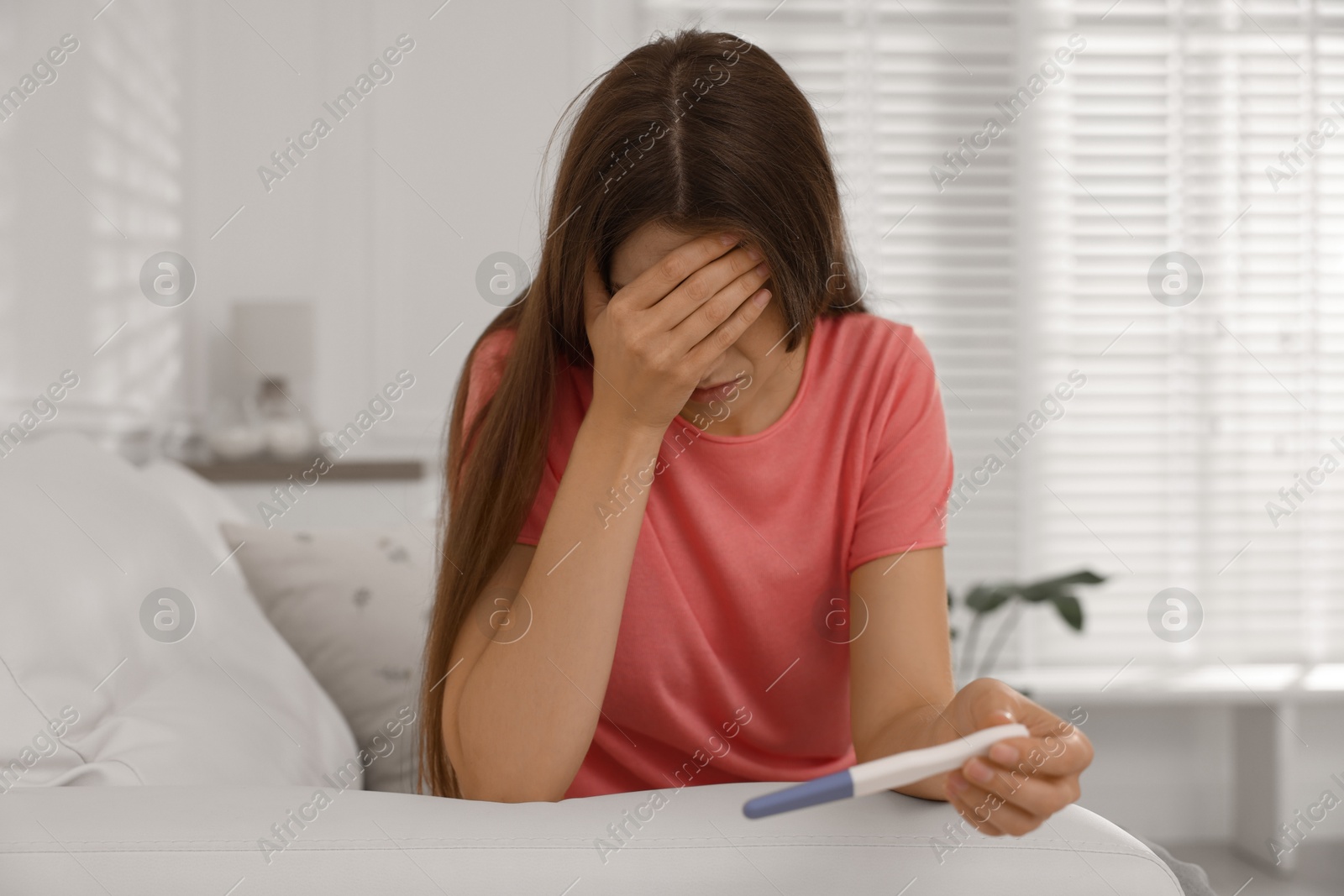 Photo of Upset woman with negative pregnancy test on sofa at home