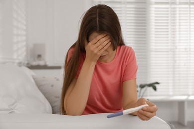 Photo of Upset woman with negative pregnancy test on sofa at home