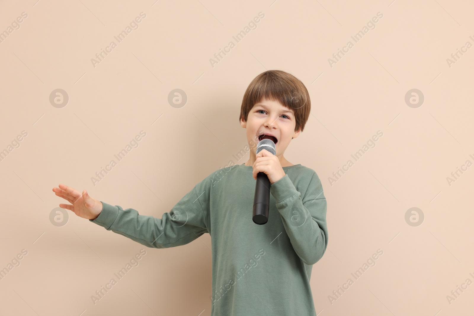 Photo of Cute boy with microphone singing near beige wall