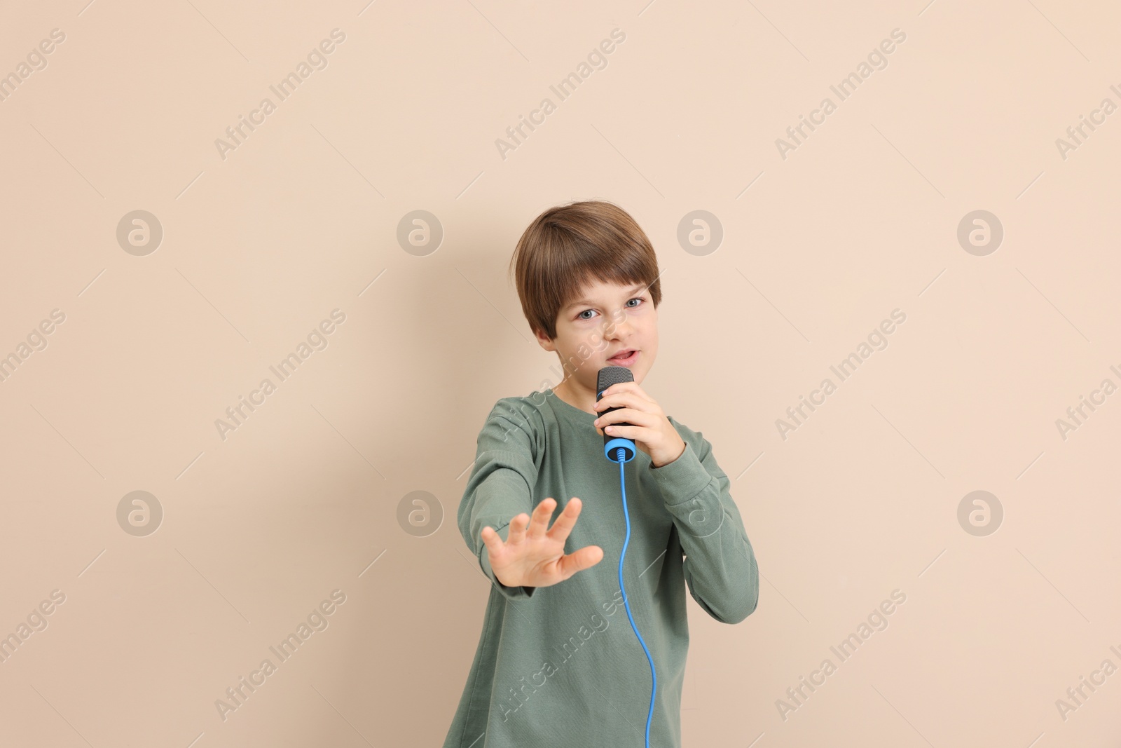 Photo of Cute boy with microphone singing near beige wall